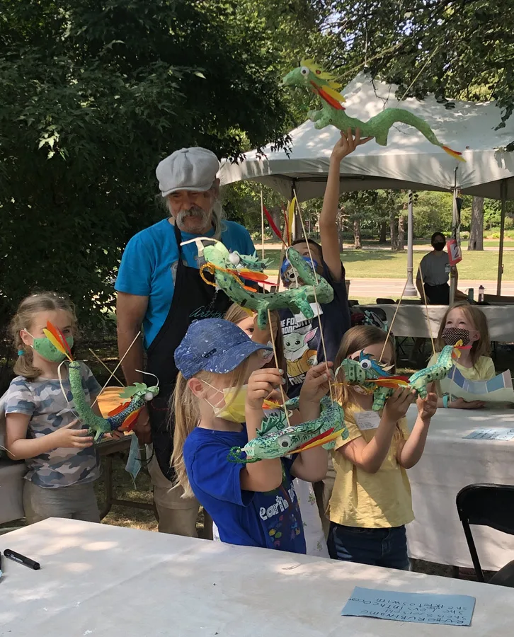 Children holding up green paper dragon puppets they made at an ArtStart outdoor workshop