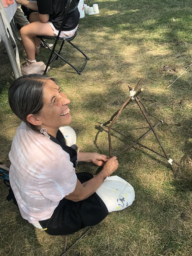 A teaching artist smiling while building a twig sculpture outdoors